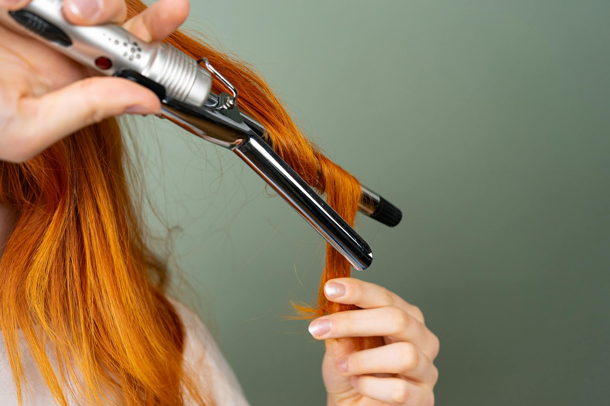Close-up of red hair being curled with a styling iron, creating beautiful curls.