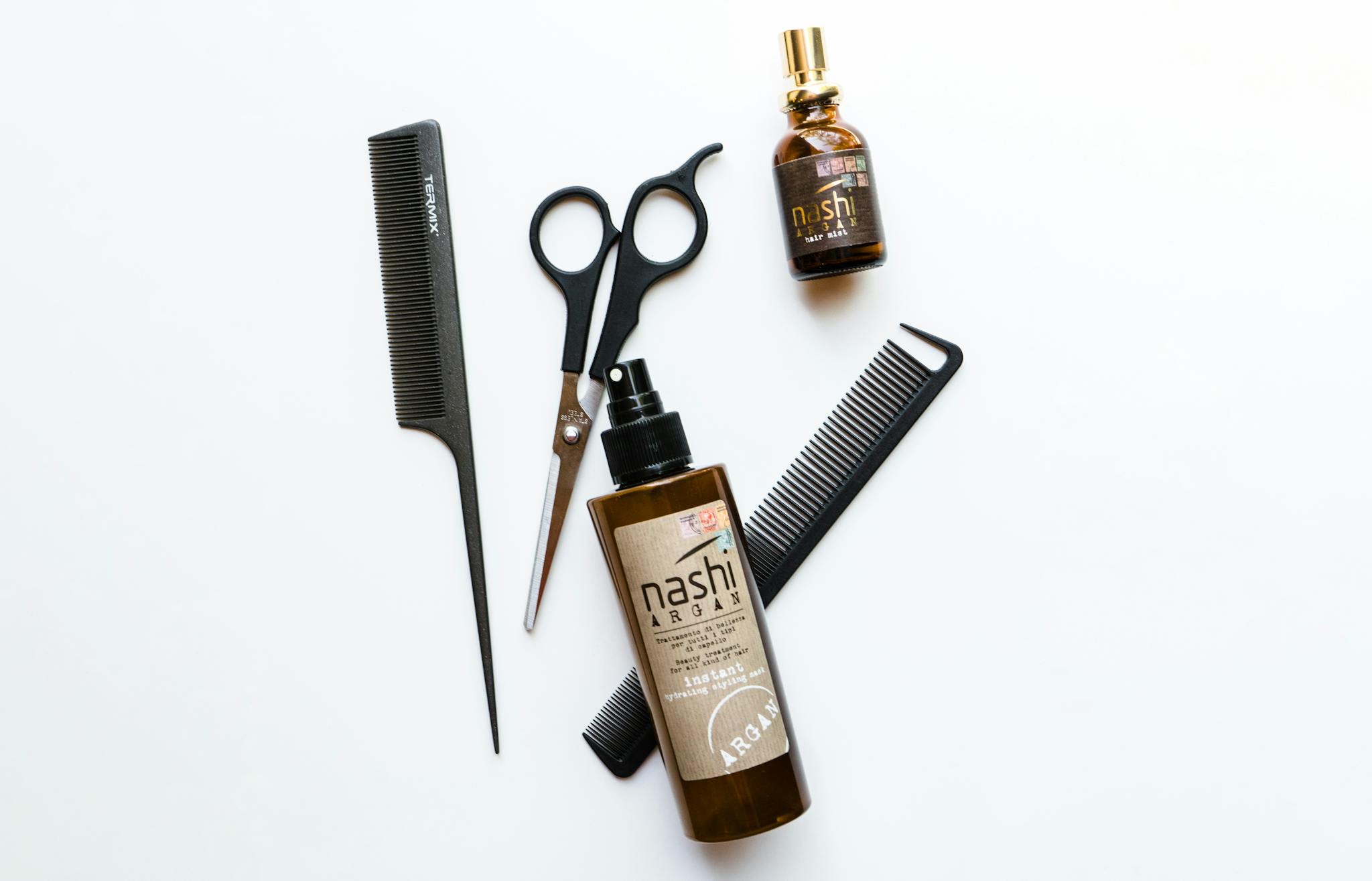 Flat lay of professional hairdressing tools with Nashi Argan oil on white background.